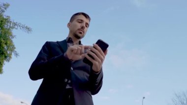  Genç ve yakışıklı bir iş adamı telefonunu kullanırken dizüstü bilgisayarını tutuyor ve sokakta dikiliyor.