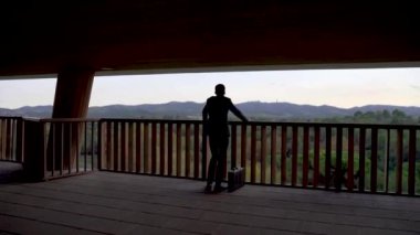 Takım elbiseli düşünceli bir işadamı ofis binasından doğa manzarasına bakıyor. Dağ dışındaki balkona bakan bir iş adamı..