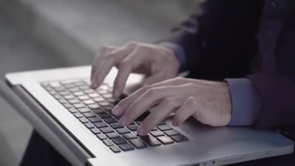 若いビジネスマンがノートパソコンを持って屋外で働いている階段に座っている 距離がある スーツを着た隔離された男 — ストック動画