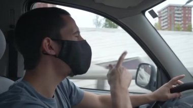 Korunaklı steril tıbbi maskeli genç adam araba sürüyor, dans ediyor ve şarkı söylüyor. Eğlenceli yolculuk, ulaşım ve araç konsepti. Karantina şehrinde salgın. Coronavirus konsepti. 