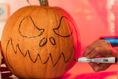 Cadılar bayramı balkabağı kabağı şeklindeki korkunç yüzü mutfakta mum ışığında çizip kesiyor. Cadılar Bayramı konsepti.