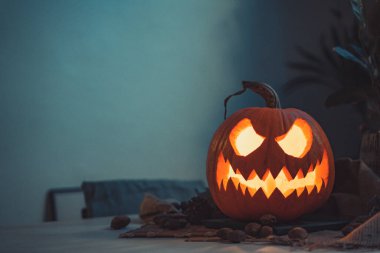 Geceleri masada mum ışığında yanan Cadılar Bayramı hayaleti kabak suratlı. İskelet, mum, fındık. Teal ve turuncu güzel natürmort.