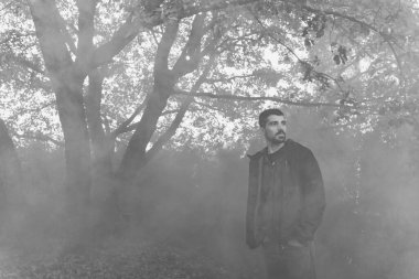 Yakışıklı genç adam sonbahar güneşli sabahında sisli ormanda tek başına yürüyor. Sıcak vintage renkler.