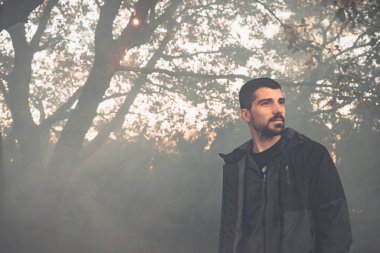 Yakışıklı genç adam sonbahar güneşli sabahında sisli ormanda tek başına yürüyor. Sıcak vintage renkler.