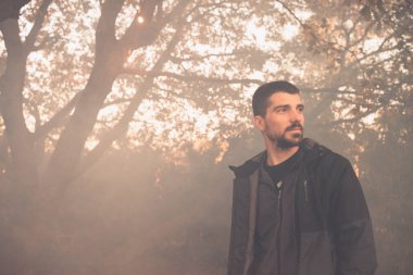 Yakışıklı genç adam sonbahar güneşli sabahında sisli ormanda tek başına yürüyor. Sıcak vintage renkler.