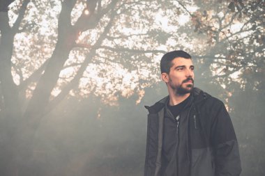 Yakışıklı genç adam sonbahar güneşli sabahında sisli ormanda tek başına yürüyor. Sıcak vintage renkler.