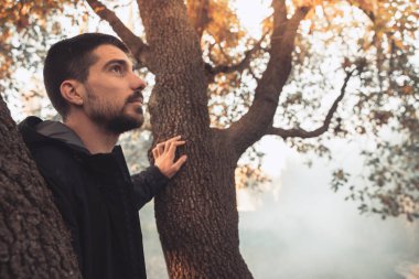 Yakışıklı genç adam sonbahar güneşli sabahında sisli ormanda tek başına yürüyor. Sıcak vintage renkler.