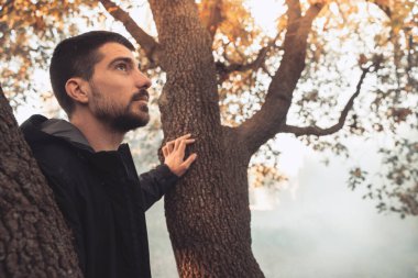 Yakışıklı genç adam sonbahar güneşli sabahında sisli ormanda tek başına yürüyor. Sıcak vintage renkler.