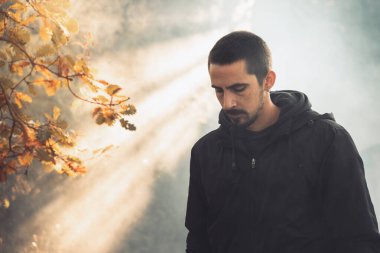 Yakışıklı genç adam sonbahar güneşli sabahında sisli ormanda tek başına yürüyor. Sıcak vintage renkler.