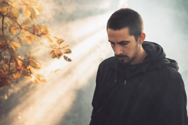 Yakışıklı genç adam sonbahar güneşli sabahında sisli ormanda tek başına yürüyor. Sıcak vintage renkler.