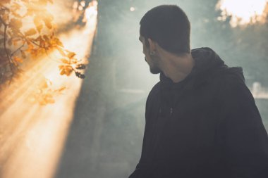 Yakışıklı genç adam sonbahar güneşli sabahında sisli ormanda tek başına yürüyor. Sıcak vintage renkler.