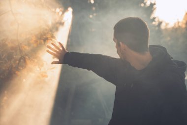 Yakışıklı genç adam sonbahar güneşli sabahında sisli ormanda tek başına yürüyor. Sıcak vintage renkler.