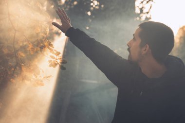 Yakışıklı genç adam sonbahar güneşli sabahında sisli ormanda tek başına yürüyor. Sıcak vintage renkler.