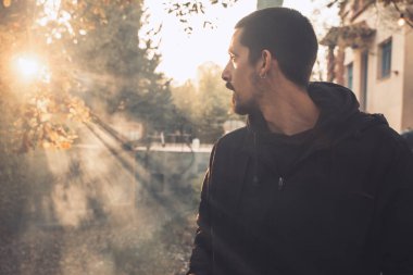 Yakışıklı genç adam sonbahar güneşli sabahında sisli ormanda tek başına yürüyor. Sıcak vintage renkler.