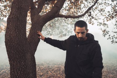 Yakışıklı genç adam sonbahar güneşli sabahında sisli ormanda tek başına yürüyor. Sıcak vintage renkler.