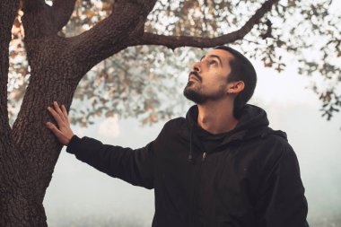 Yakışıklı genç adam sonbahar güneşli sabahında sisli ormanda tek başına yürüyor. Sıcak vintage renkler.