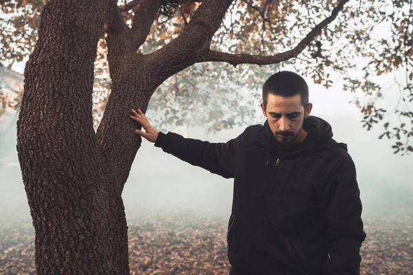 Yakışıklı genç adam sonbahar güneşli sabahında sisli ormanda tek başına yürüyor. Sıcak vintage renkler.