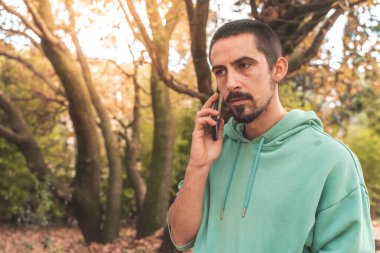 Coronavirus. Koronavirüs yüzünden karantinada olan bir adam sonbaharda açık havada cep telefonu kullanarak koruyucu maske takıyor. Evde kal. Video çağrısı. 