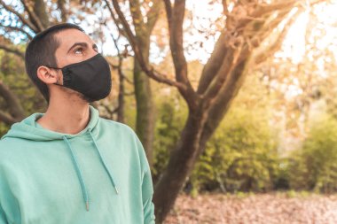 Coronavirus. Koronavirüs yüzünden karantinada olan bir adam sonbaharda koruyucu maske takıyor ve kaput takıyor. Evde kal..