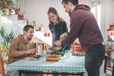 Friends having fun during dinner at dining table. Cheerful young people eating, toasting and enjoying with friends at home.