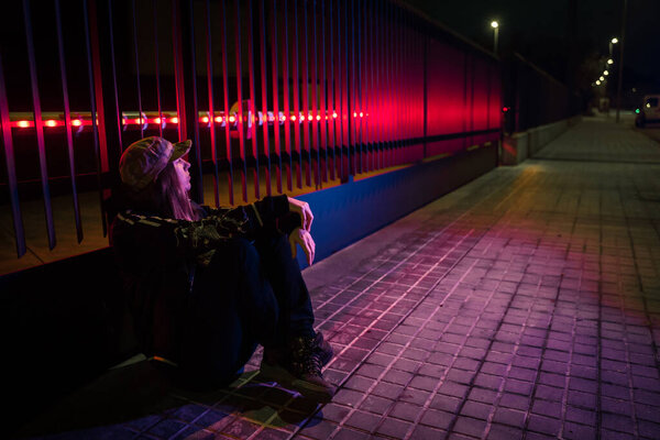 Beautiful cinematic portrait of stylish young woman in neon lighted fence. Bright neoned colors. Caucasian model, musician outdoors. Youth culture and music concept.