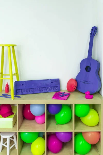Pop colorful objects, toys and instruments on a wooden shelf. Party vivid color objects and balloons.