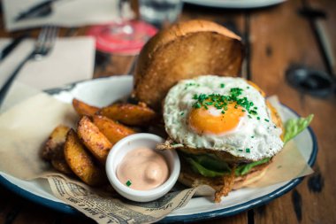 Susamlı ekmeğin içinde bütün gün kahvaltılık burger, kızarmış yumurta ve pastırma. Hippi yemeği. Metin için kopyalama alanı olan yiyecek pornosu.