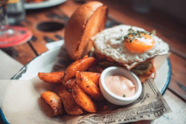 Susamlı ekmeğin içinde bütün gün kahvaltılık burger, kızarmış yumurta ve pastırma. Hippi yemeği. Metin için kopyalama alanı olan yiyecek pornosu.