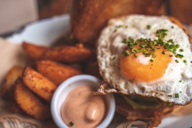 Susamlı ekmeğin içinde bütün gün kahvaltılık burger, kızarmış yumurta ve pastırma. Hippi yemeği. Metin için kopyalama alanı olan yiyecek pornosu.