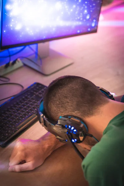 Professional gamer defeated, exhausted and sad in front of his personal computer. Room lit by Neon Lights in Retro Arcade Style. Cyber Championship. Footage fade out into bokeh.