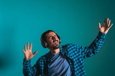 Dans eden ve şarkı söyleyen genç yakışıklı adam mavi bir arka planda kulaklıkla müzik dinliyor. Müzikten hoşlanan mutlu erkek.