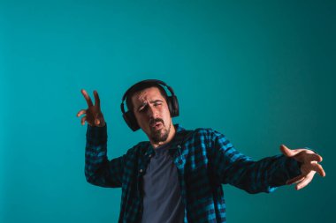 Dans eden ve şarkı söyleyen genç yakışıklı adam mavi bir arka planda kulaklıkla müzik dinliyor. Müzikten hoşlanan mutlu erkek.