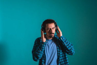 Dans eden ve şarkı söyleyen genç yakışıklı adam mavi bir arka planda kulaklıkla müzik dinliyor. Müzikten hoşlanan mutlu erkek.