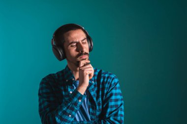 Dans eden ve şarkı söyleyen genç yakışıklı adam mavi bir arka planda kulaklıkla müzik dinliyor. Müzikten hoşlanan mutlu erkek.