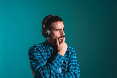 Dans eden ve şarkı söyleyen genç yakışıklı adam mavi bir arka planda kulaklıkla müzik dinliyor. Müzikten hoşlanan mutlu erkek.