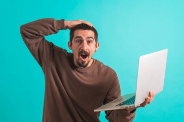 Laptop bilgisayarı olan genç ve yakışıklı bir adam mavi arka planda izole edilmiş. Metin için alanı kopyala.