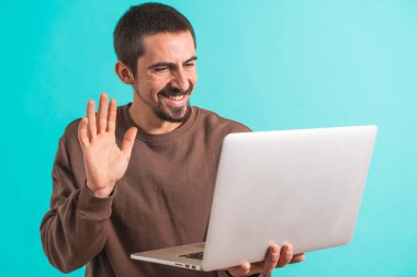 Laptop bilgisayarıyla konuşan genç yakışıklı bir adam mavi arka plandan izole edilmiş bir video görüşmesiyle konuşuyor. Metin için alanı kopyala.