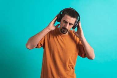 Dans eden ve şarkı söyleyen genç yakışıklı adam mavi bir arka planda kulaklıkla müzik dinliyor. Müzikten hoşlanan mutlu erkek.