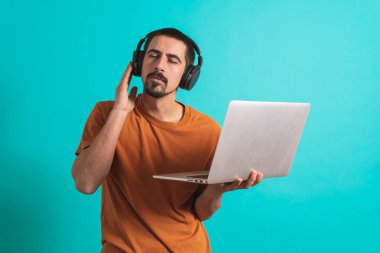 Dans eden ve şarkı söyleyen genç yakışıklı adam mavi bir arka planda kulaklıkla müzik dinliyor. Müzikten hoşlanan mutlu erkek.