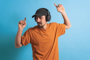 Dans eden ve şarkı söyleyen genç yakışıklı adam mavi bir arka planda kulaklıkla müzik dinliyor. Müzikten hoşlanan mutlu erkek.