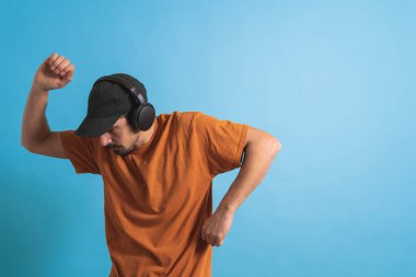 Dans eden ve şarkı söyleyen genç yakışıklı adam mavi bir arka planda kulaklıkla müzik dinliyor. Müzikten hoşlanan mutlu erkek.