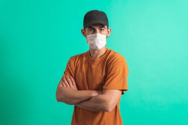 Cerrahi maskesiyle kameraya bakan yakışıklı bir gencin portresi. Mavi arka planda izole edilmiş kapalı stüdyo görüntüleri..