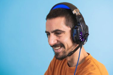 Oyun kulaklığı olan genç yakışıklı bir adam oyun oynayan dizüstü bilgisayarla mavi arka planda izole edilmiş..