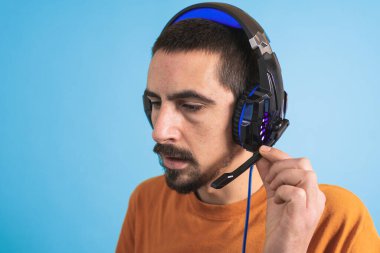 Oyun kulaklığı olan genç yakışıklı bir adam oyun oynayan dizüstü bilgisayarla mavi arka planda izole edilmiş..