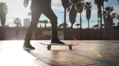 Genç havalı milenyum adamı, genç hippi kaykayıyla sahil şeridinde geziyor. Sinematografik aksiyon geniş çekim erkek kaykay numaraları yapmak Güneşli bir günde turistik bölgede.