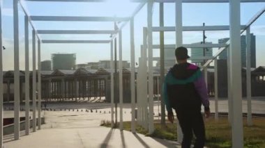 Genç havalı milenyum adamı, genç hippi kaykayıyla sahil şeridinde geziyor. Sinematografik aksiyon geniş çekim erkek kaykay numaraları yapmak Güneşli bir günde turistik bölgede.