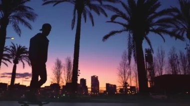 Genç havalı milenyum adamı, genç hippi kaykayıyla sahil şeridinde geziyor. Sinematografik aksiyon geniş çekim erkek kaykay numaraları yapmak Güneşli bir günde turistik bölgede.