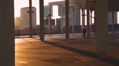 Genç havalı milenyum adamı, genç hippi kaykayıyla sahil şeridinde geziyor. Sinematografik aksiyon geniş çekim erkek kaykay numaraları yapmak Güneşli bir günde turistik bölgede.