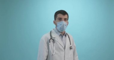 Tıbbi maskeli bir erkek doktor mavi arka planda Corona virüsü aşısı olan bir şırınga tutuyor. Grip, kızamık, koronavirüs aşısı aşısı aşısı. Coronavirus aşısı.