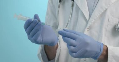 Tıbbi maskeli bir erkek doktor mavi arka planda Corona virüsü aşısı olan bir şırınga tutuyor. Grip, kızamık, koronavirüs aşısı aşısı aşısı. Coronavirus aşısı. 